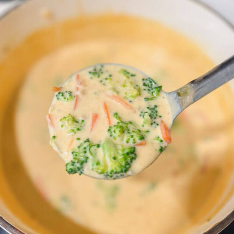 a close up of a ladle of Panera's copycat broccoli cheddar soup being held over a white pot of the soup.