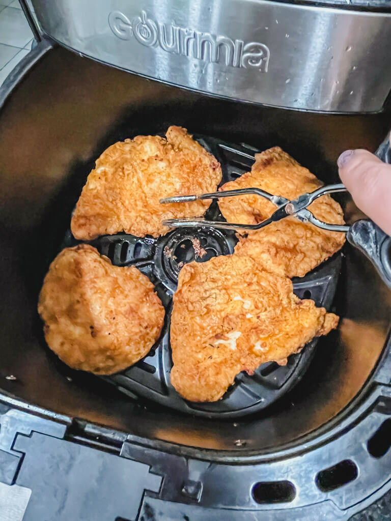 me holding a pair of tongs flipping the chicken over in the air fryer basket.