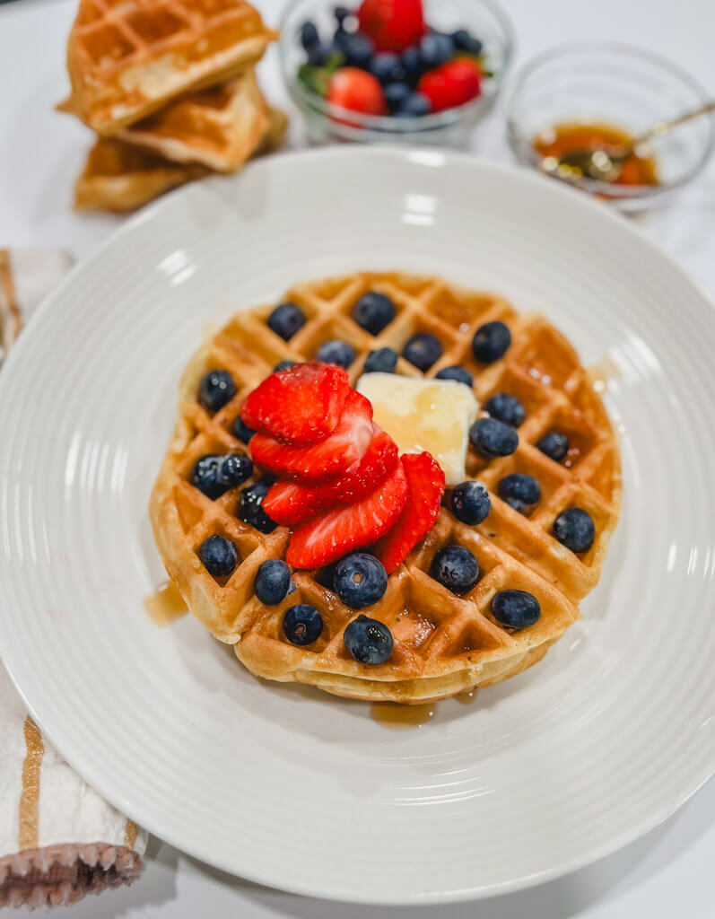 a buttery belgian waffle with fresh berries on a white plate.