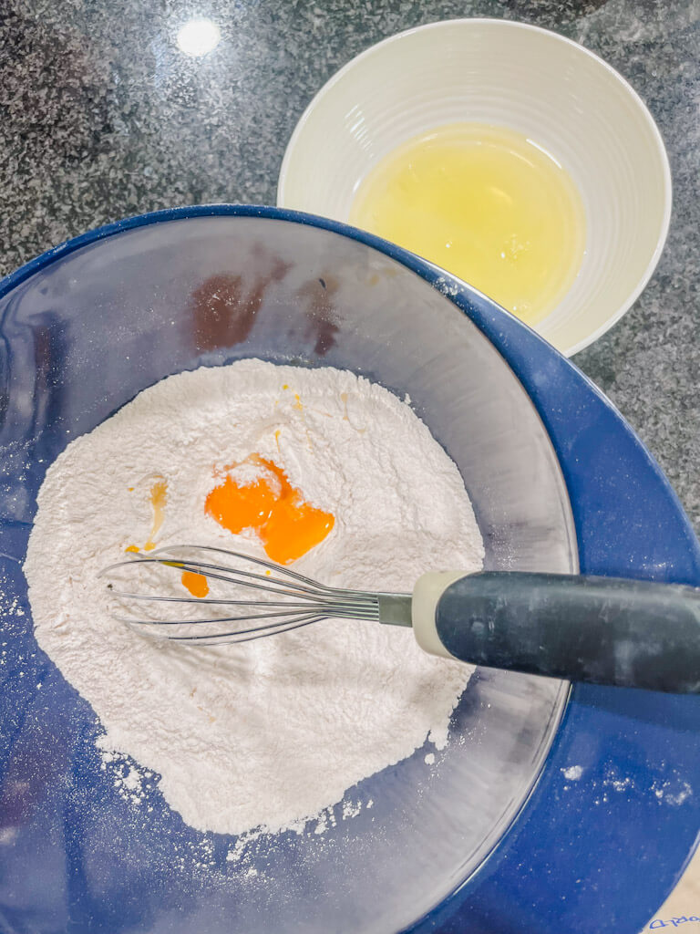 two egg yolks added to the blue mixing bowl, with a side of egg whites in a white bowl. 