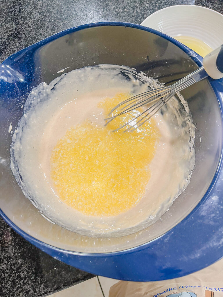 melted butter and milk added to a blue mixing bowl for buttery waffle recipe.