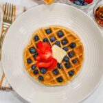 a buttery waffle on a white plate with fresh berries and a pat of butter on top.