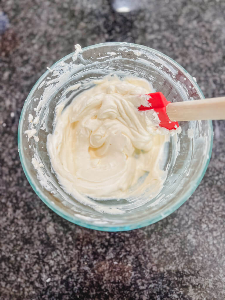 cream cheese mixture in a clear glass bowl with a red spatula.