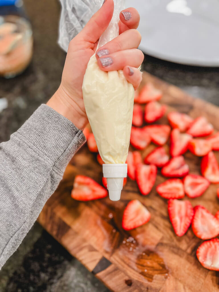 a piping bag filled with cream cheese mixture being held over halved strawberries.