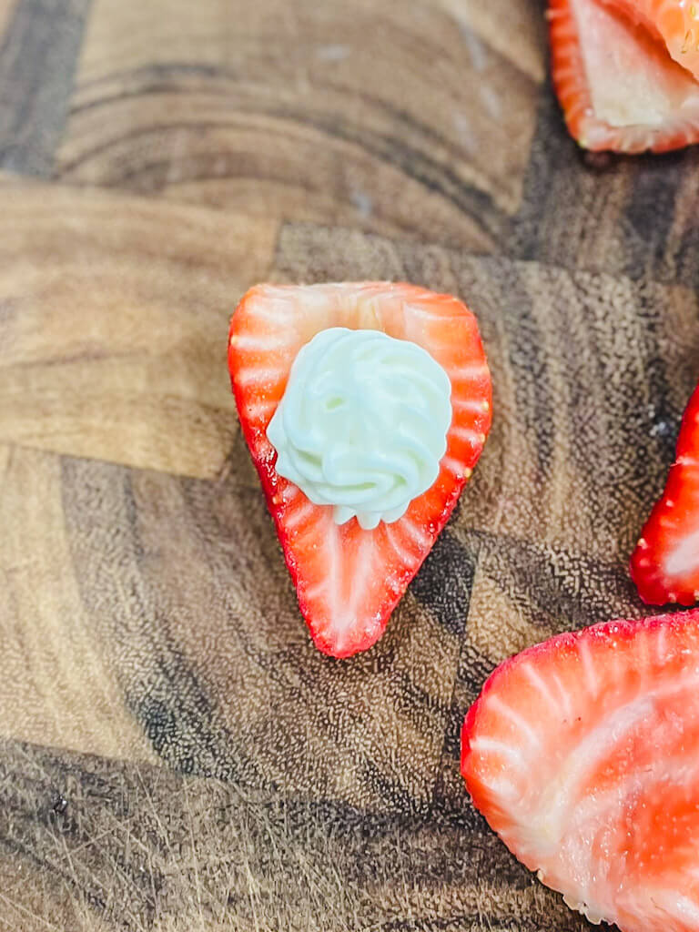 a strawberry filled with cream cheese filling on a wooden cutting board.