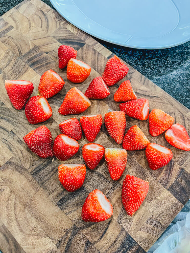 fresh strawberries on a wooden cutting board with the leaves cut off.