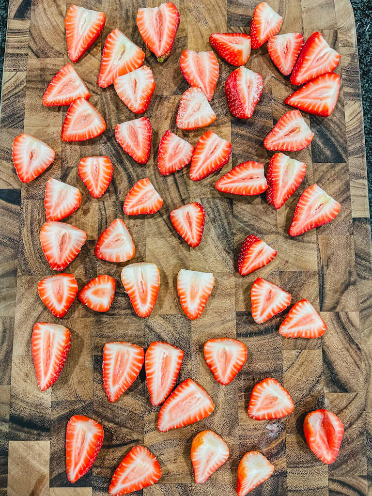 2 dozen strawberries sliced in half lengthwise on a wooden cutting board for deviled strawberries tiktok recipe.