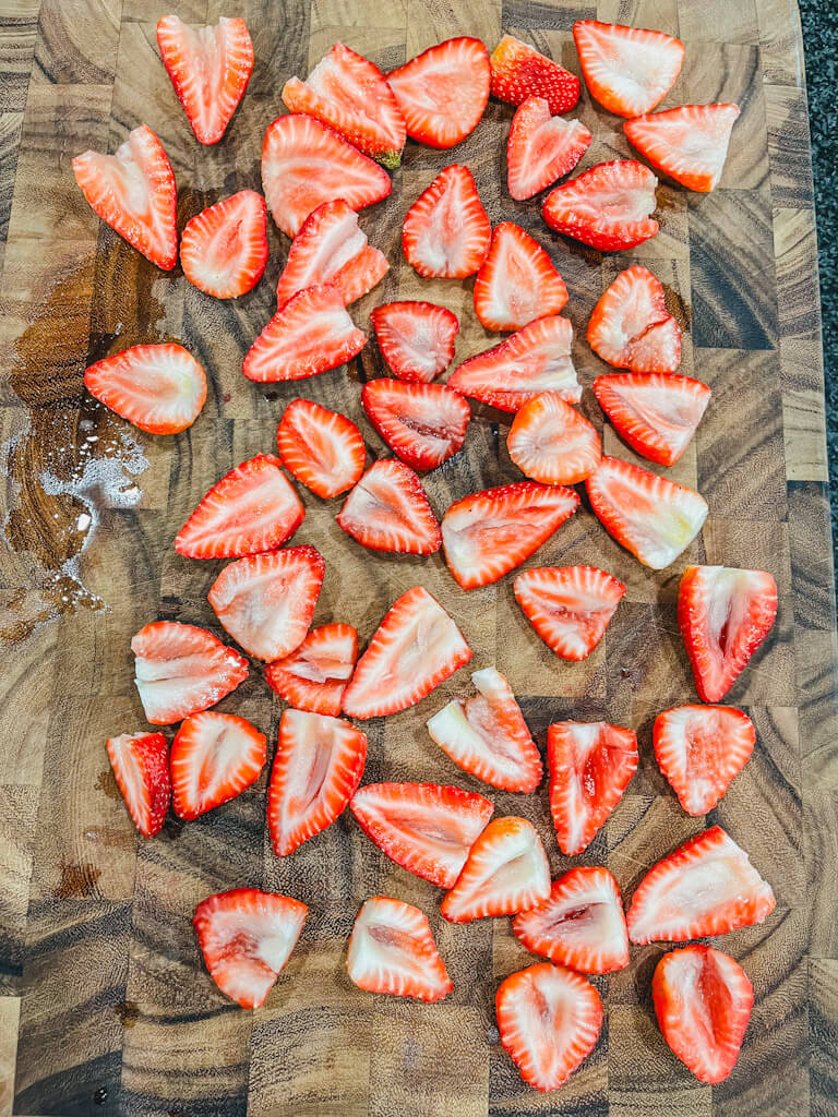 hulled sliced strawberries on a wooden cutting board.