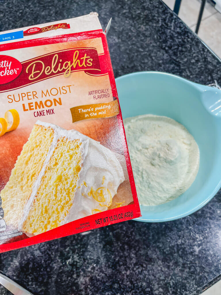 a box of lemon cake mix being held over a mixing bowl.