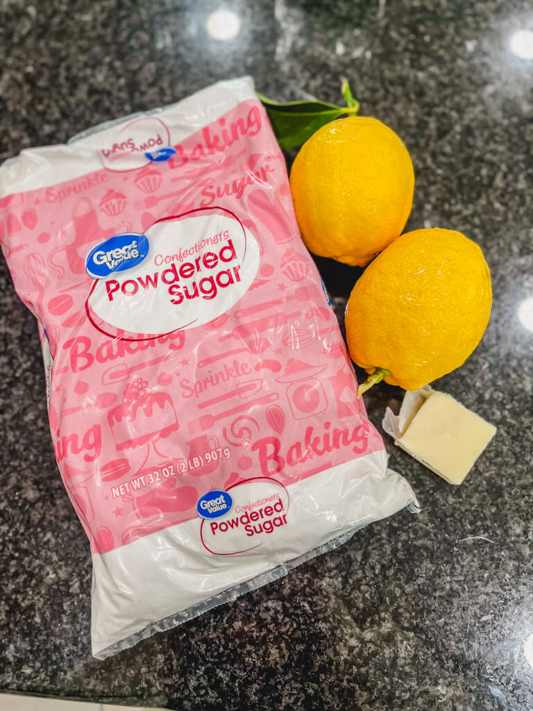 ingredients for lemon icing laid out on a black countertop.
