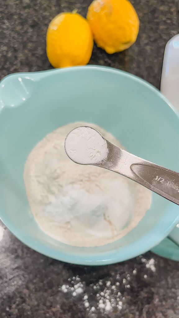 1/2 teaspoon of baking powder being added to the other dry ingredients in a blue mixing bowl.