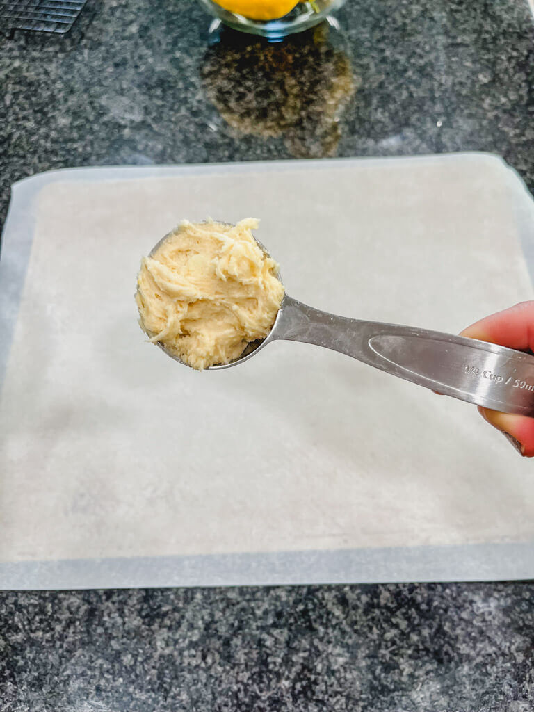 1/4 cup measuring cup holding lemon cookie dough about to be placed onto cookie sheet.