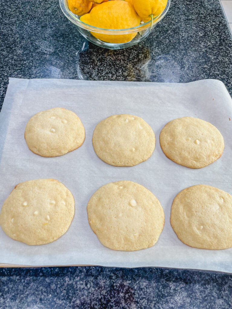 6 baked lemon drop cookies cooling after baking on a black counter.