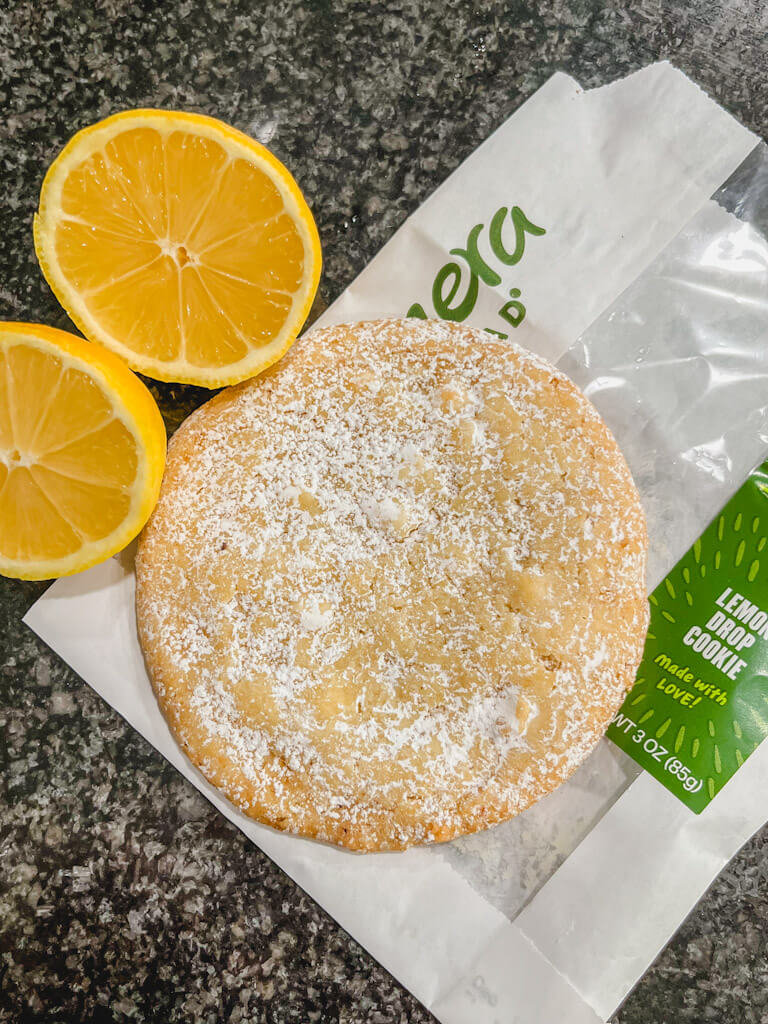 a panera lemon drop cookie on a bag with a sliced lemon next to the cookie.