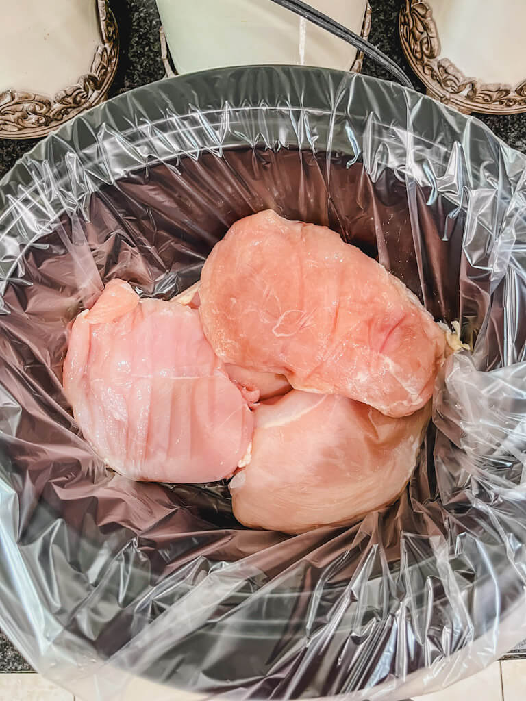 chicken breasts in a slow cooker with a crockpot liner.
