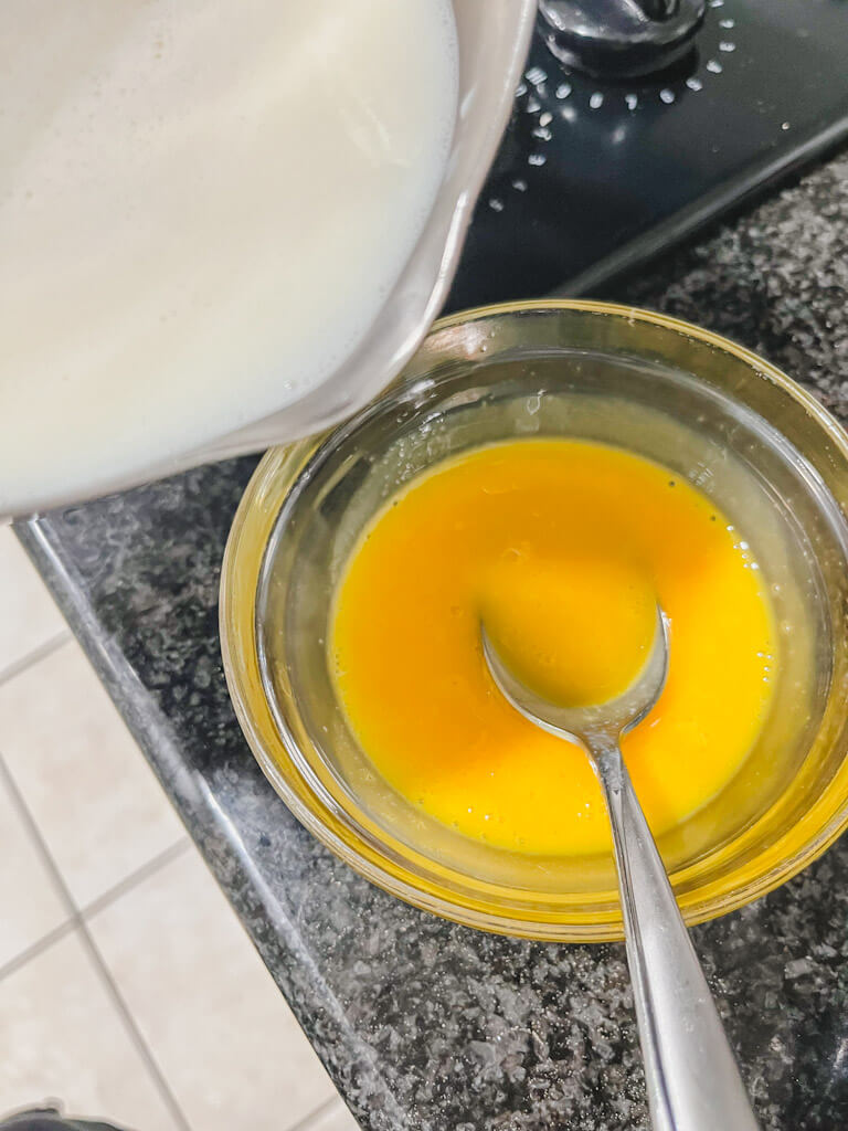 whisked egg yolks in a small glass bowl with the hot milk about to be added to the yolks.