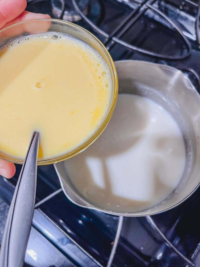 egg yolks mixed with hot milk about to be added to saucepan with hot milk and sugar mixture.