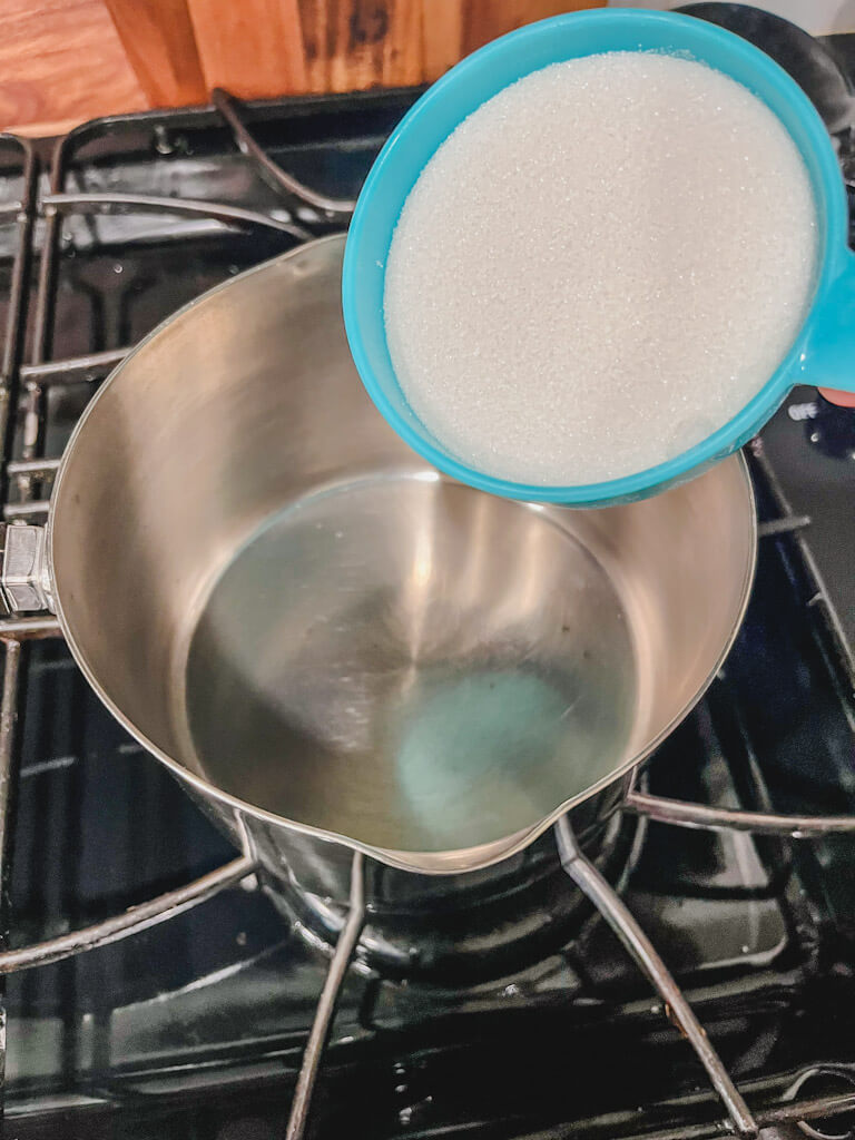 sugar in a blue measuring cup about to be poured into a saucepan.