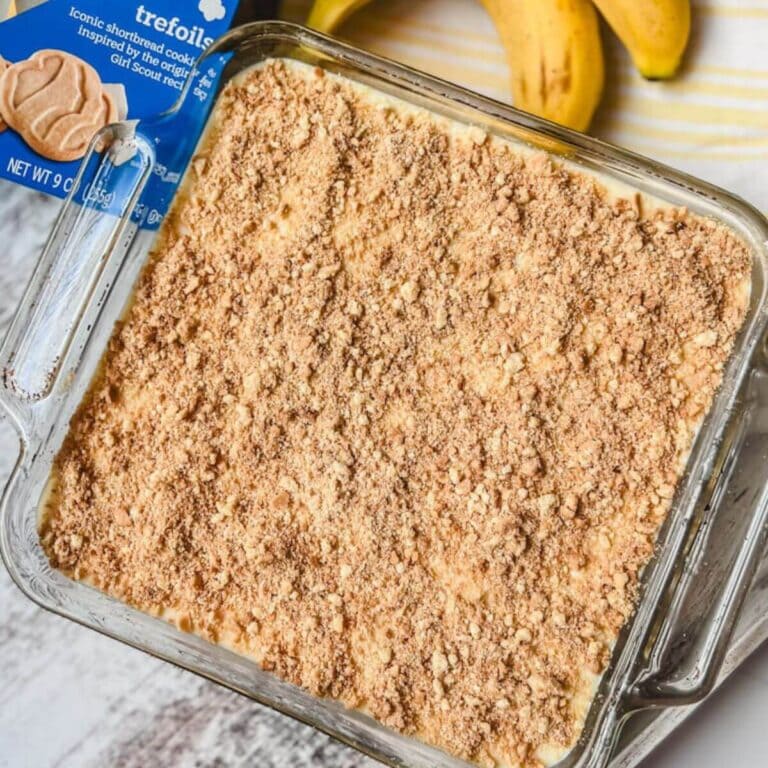 overhead view of banana pudding made with trefoils in a glass baking dish next to a box of girl scout cookies and bananas.