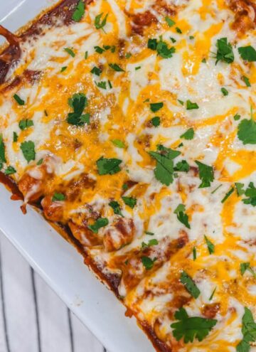 close up of creamy chicken enchiladas made with flour tortillas in a white baking dish.