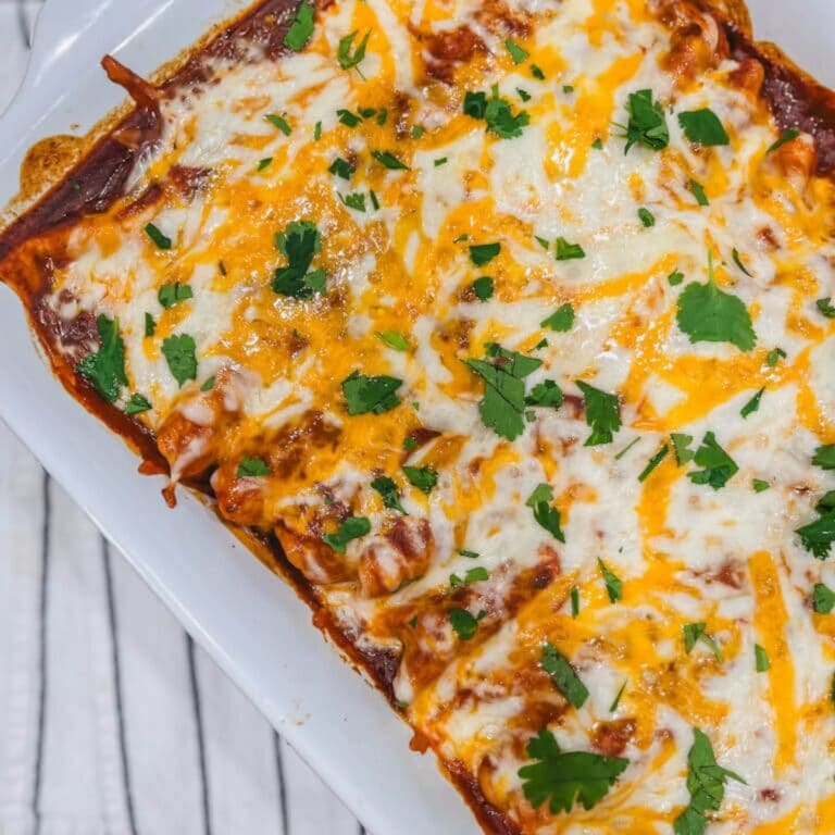 close up of creamy chicken enchiladas made with flour tortillas in a white baking dish.