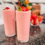 panera strawberry banana smoothie in a tall clear glass with a fresh strawberry on top.