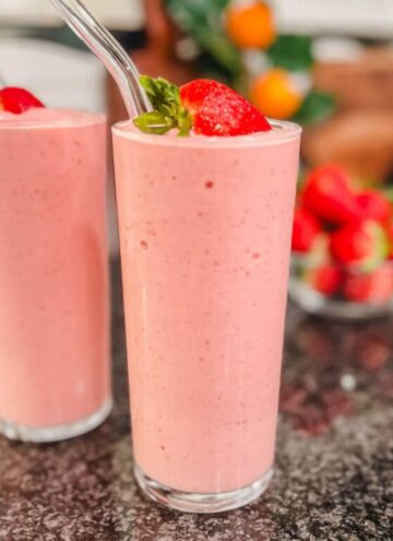 panera strawberry banana smoothie in a tall clear glass with a fresh strawberry on top.