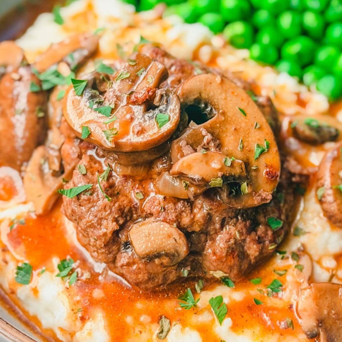 close up of Instant Pot Salisbury Steak with Mushroom Gravy sitting on top of mashed potatoes with green peas in the background.