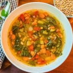 close up view of a bowl of lentil and bean soup in a white bowl with a small bowl of dried lentils next to the soup bowl.