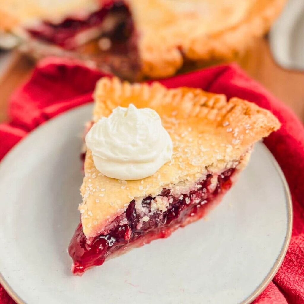 a slice of old fashioned cherry pie on a cream colored plate.