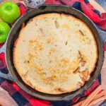 overhead view of cast iron skillet apple cobbler next to cinnamon sticks and granny smith apples.