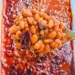 close up of a spoonful of bbq bacon beans being held over the casserole dish.