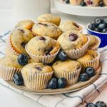 little bites blueberry muffins on a plate that is sitting on top of a blue striped kitchen towel.