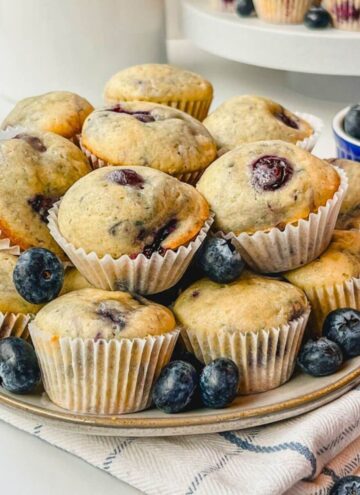little bites blueberry muffins on a plate that is sitting on top of a blue striped kitchen towel.
