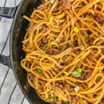 close up of Mongolian beef noodles recipe in a large cast iron skillet next to a black and white kitchen towel.