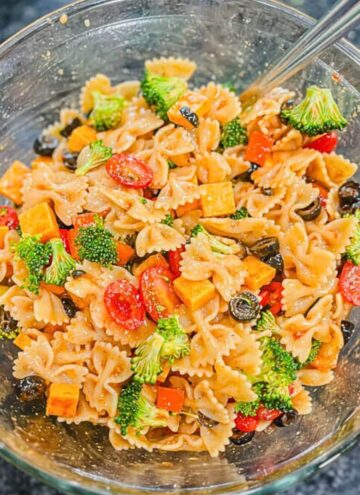 over head view of summer pasts salad in a glass bowl with a large serving spoon in the bowl.