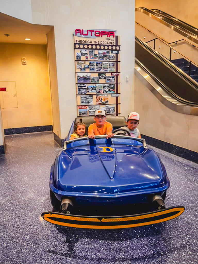 three kids sitting in a blue autopia vehicle at the Disneyland Hotel.