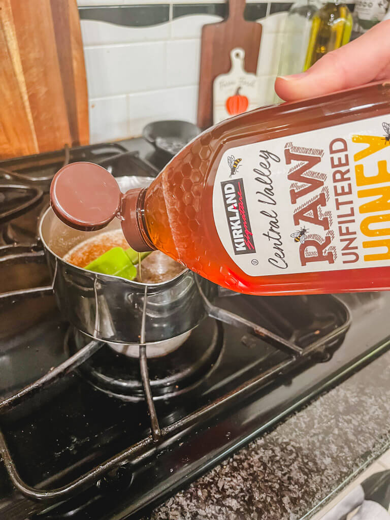 a drizzle of honey being poured into the small saucepan with brown sugar and butter.