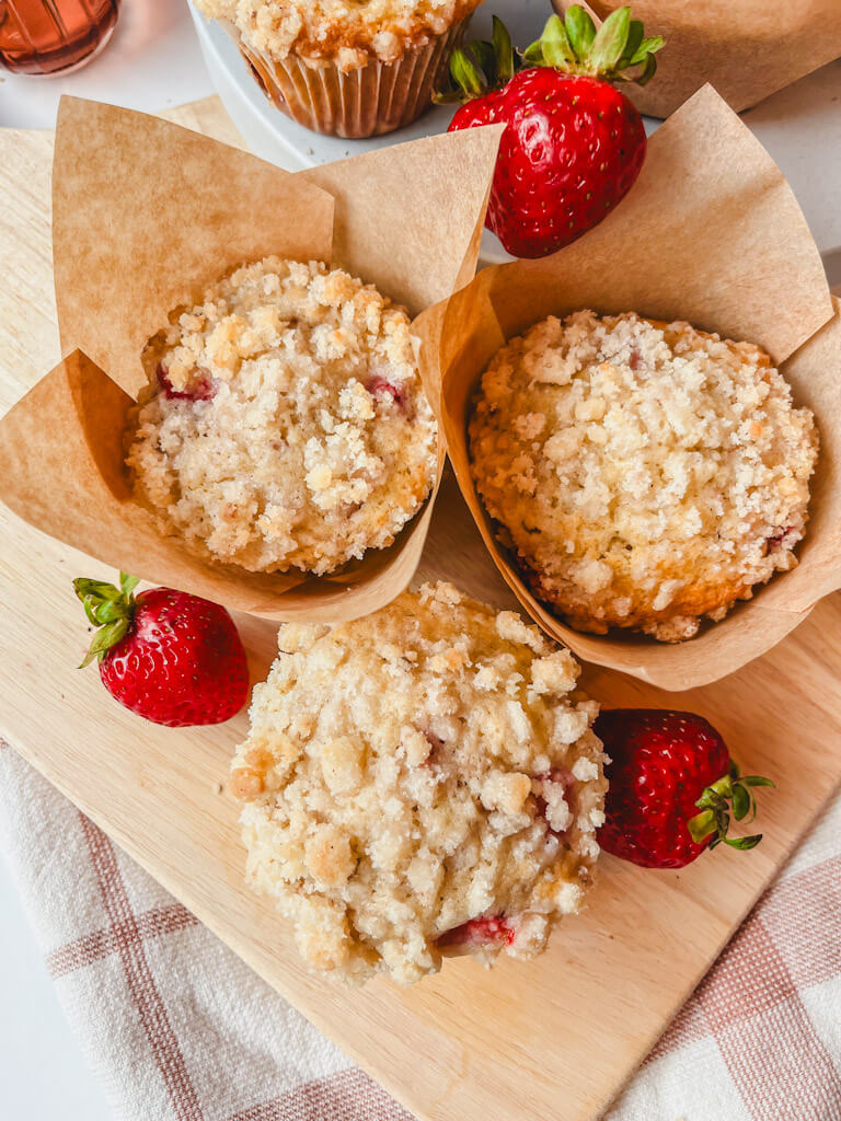 overhead view of three strawberry muffins together on a wooden cutting board.