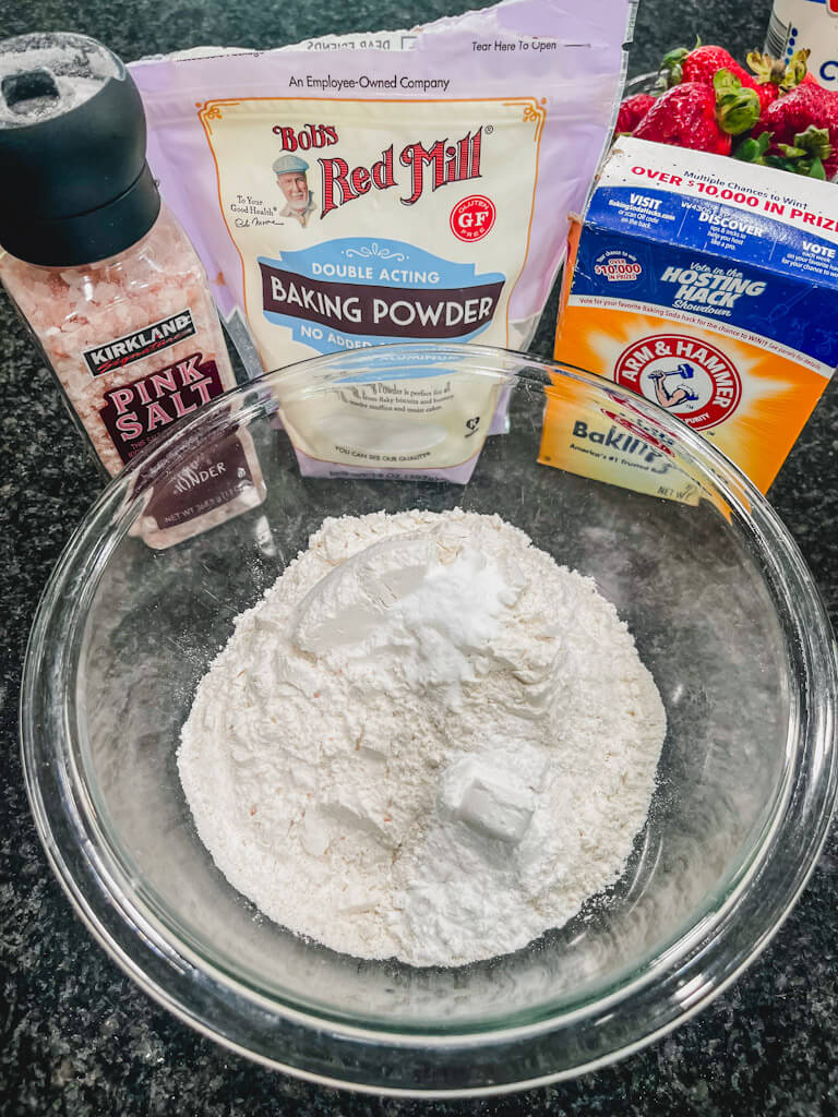 flour in a glass bowl with ingredients behind the bowl.