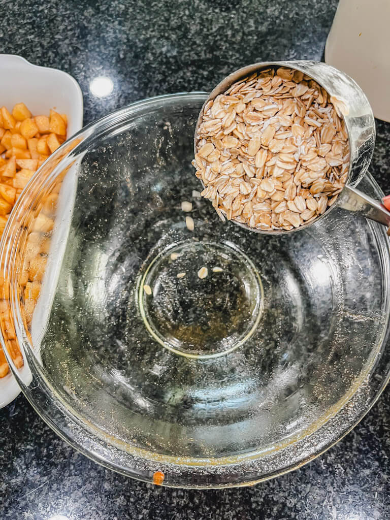 a measuring cup holding rolled oats being poured into a bowl to make the oat crumble.