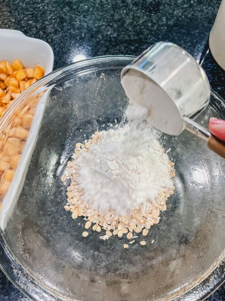 a measuring cup holding flour being added to the oats.