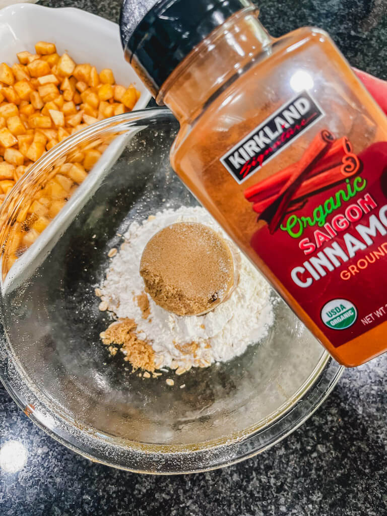 some cinnamon about to be sprinkled into the bowl with the apples in the background.