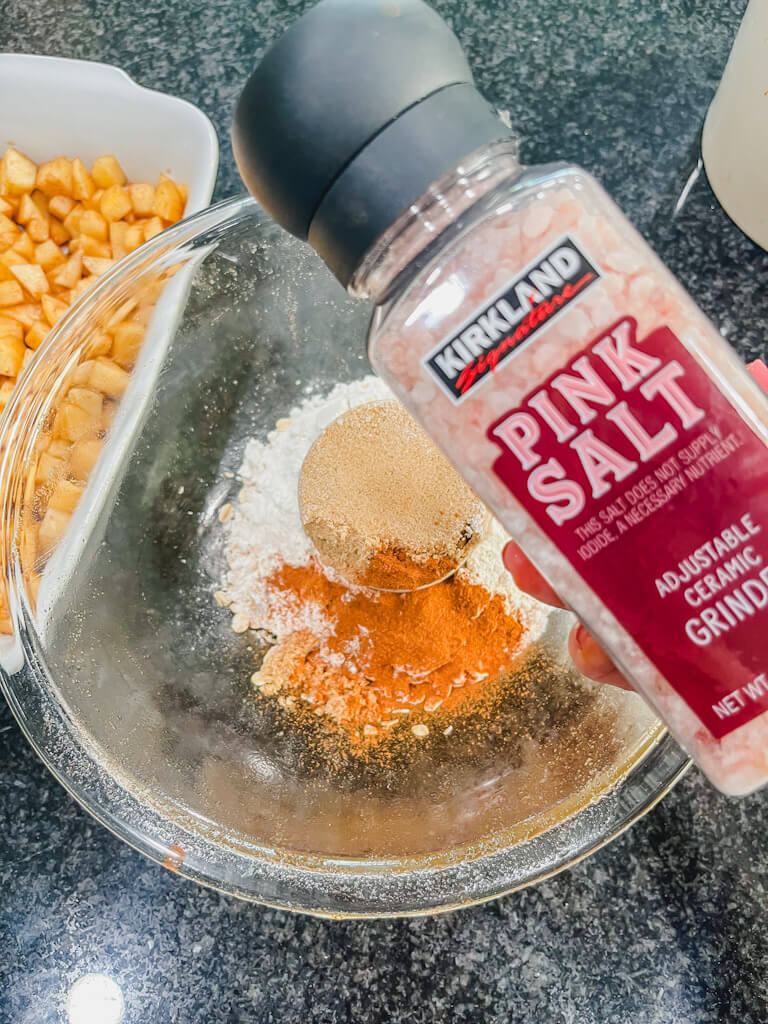salt being held over the bowl of oat crumble.