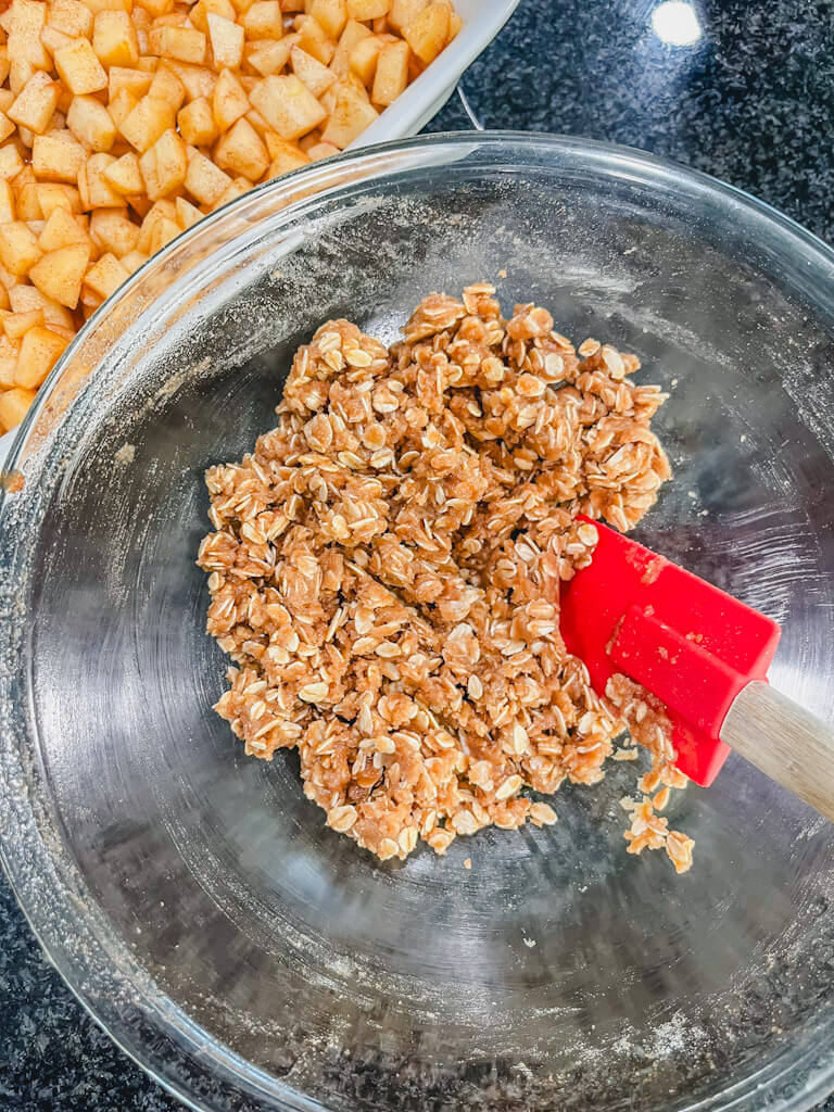 a red spatula combining the butter and oats together to resemble a crumbly, wet sand-like mixture.