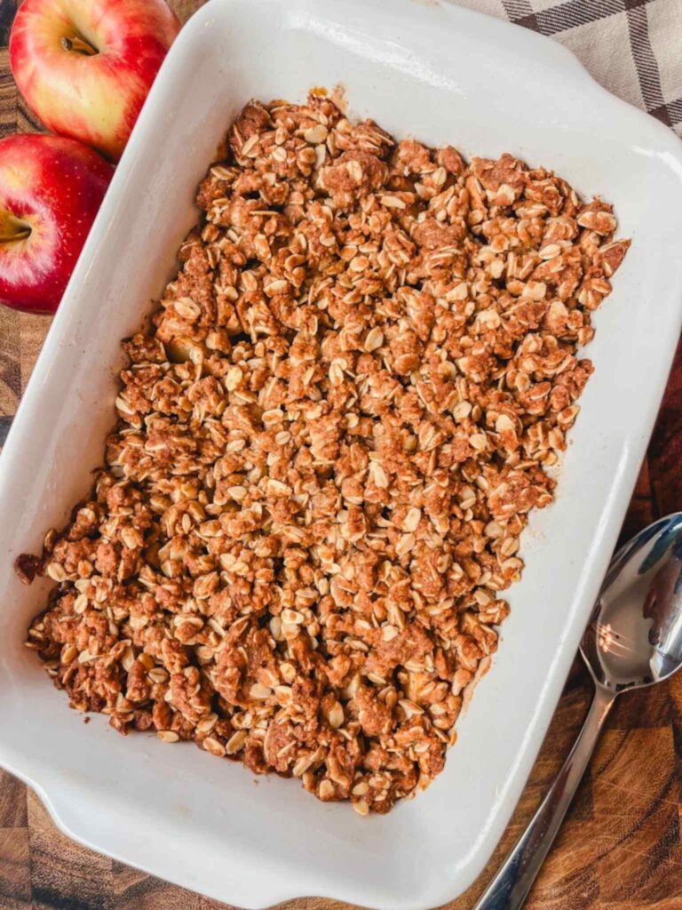 overhead view of apple crisp in a white baking dish next to a couple of apples.