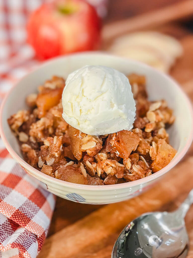 a serving of apple crisp in a small bowl with a scoop of vanilla ice cream on top.