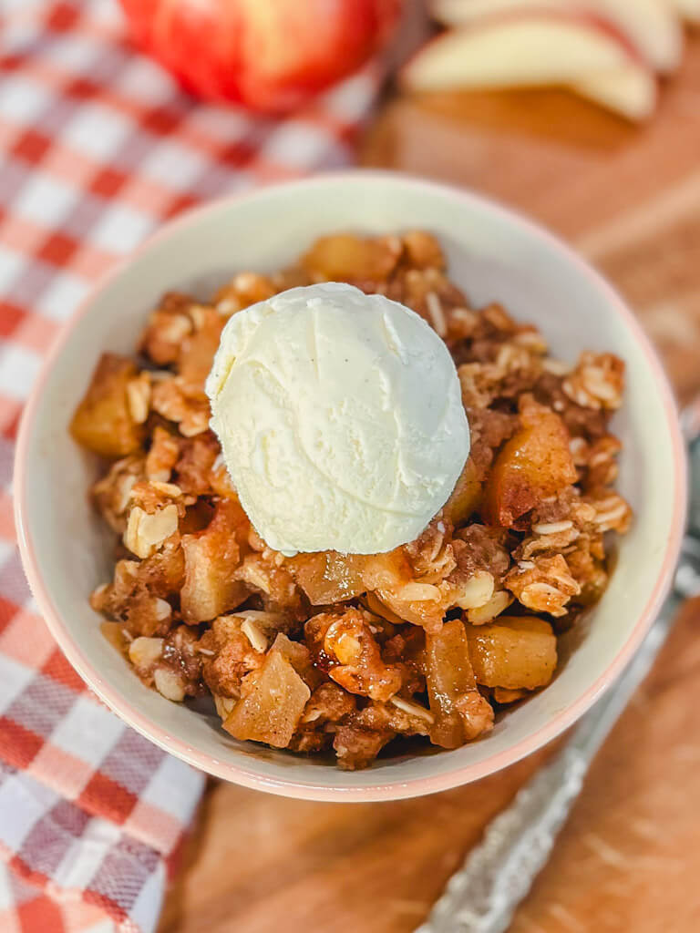 a small bowl with warm apple crisp and a scoop of ice cream next to a spoon.