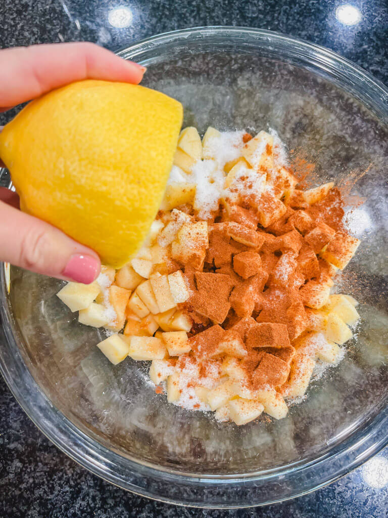half of a lemon being held over the bowl with apples for apple crisp recipe.