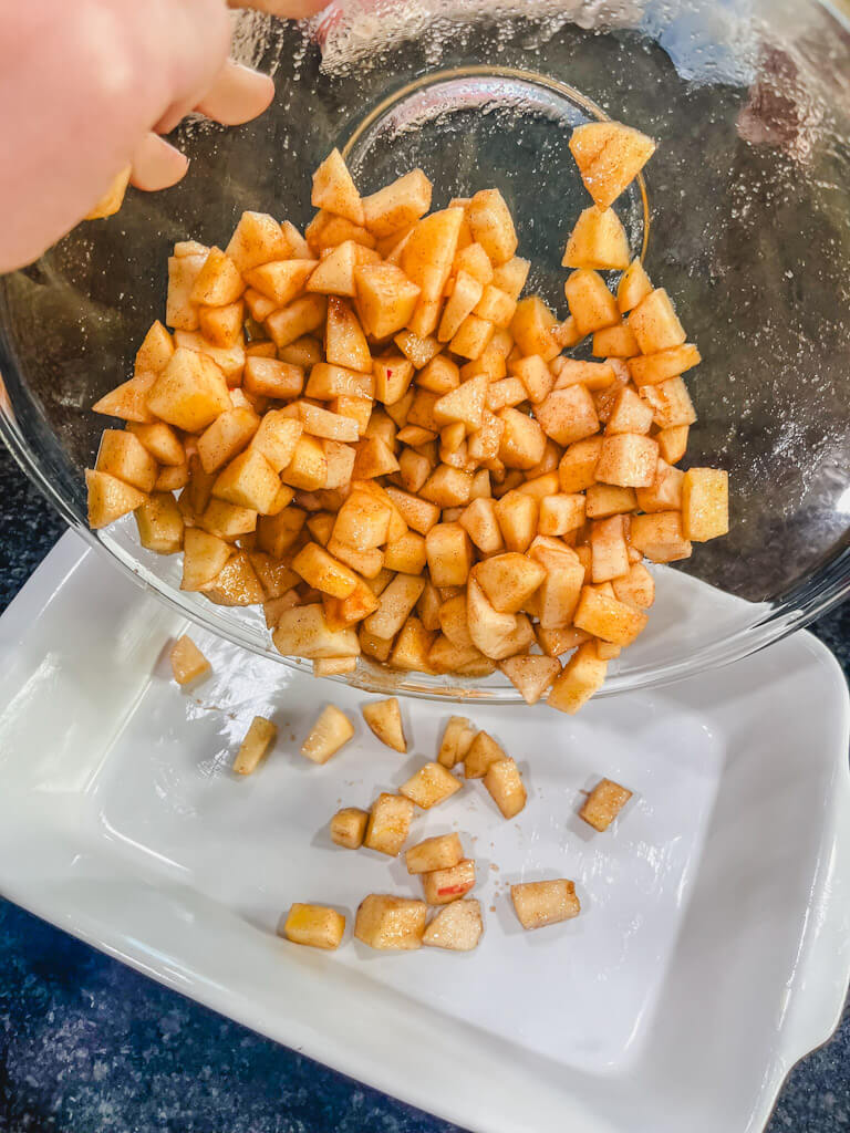 the spiced diced apples being poured into the prepared baking dish.